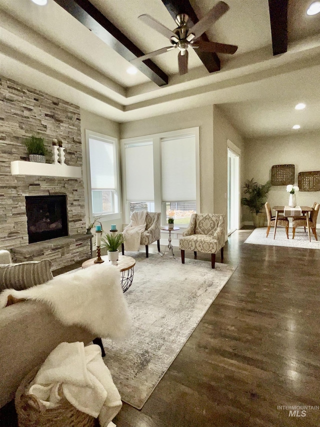 living room with a stone fireplace, dark wood-type flooring, and ceiling fan