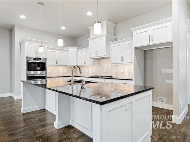 kitchen featuring decorative light fixtures, dark stone countertops, appliances with stainless steel finishes, an island with sink, and white cabinets