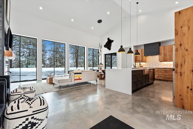 kitchen featuring pendant lighting, a kitchen island with sink, a towering ceiling, tasteful backsplash, and stainless steel dishwasher