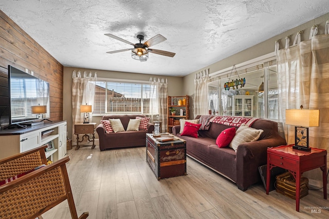 living room with light wood-style flooring, wooden walls, ceiling fan, and a textured ceiling