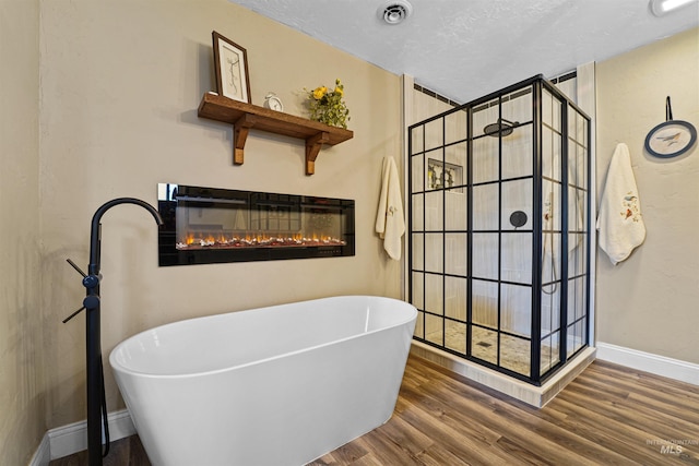 full bathroom featuring a soaking tub, visible vents, a glass covered fireplace, wood finished floors, and walk in shower