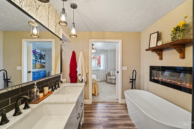 ensuite bathroom featuring a glass covered fireplace, a sink, a textured ceiling, and wood finished floors