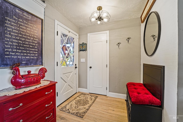 foyer entrance with light wood finished floors, a textured wall, an inviting chandelier, a textured ceiling, and baseboards