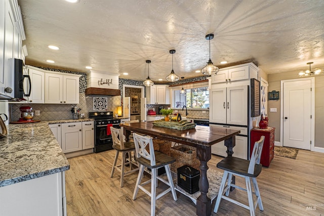 kitchen featuring black gas stove, light wood-style flooring, white cabinets, and decorative backsplash