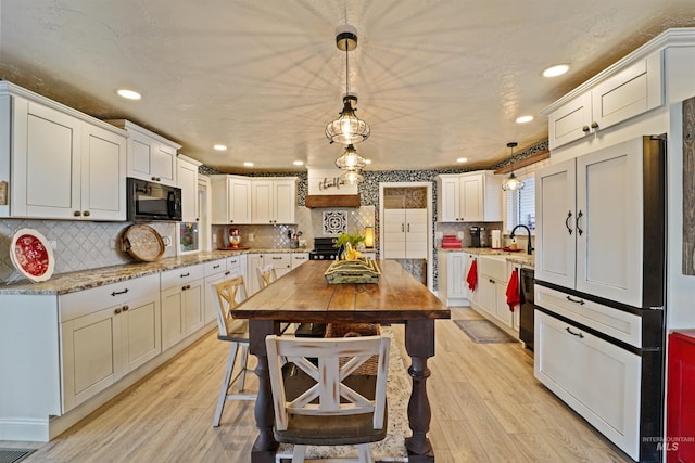 kitchen featuring pendant lighting, light wood-type flooring, black microwave, and backsplash