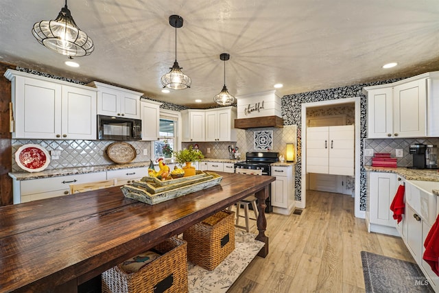 kitchen featuring white cabinets, light wood-style flooring, stainless steel stove, black microwave, and wooden counters