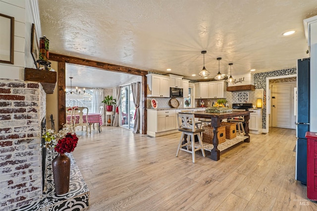 kitchen with black microwave, light wood finished floors, a textured ceiling, and tasteful backsplash