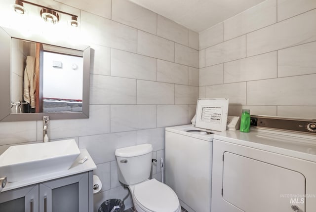half bathroom with separate washer and dryer, tile walls, toilet, and vanity