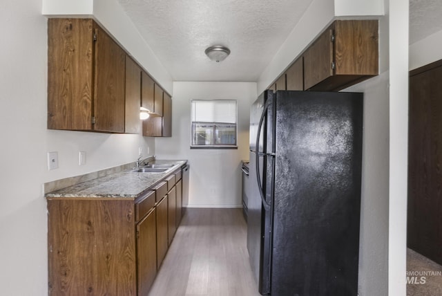 kitchen with a sink, freestanding refrigerator, a textured ceiling, light wood-style flooring, and baseboards