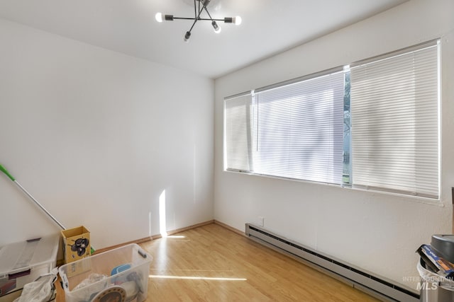 unfurnished room featuring a chandelier, light wood-style flooring, baseboards, and a baseboard heating unit
