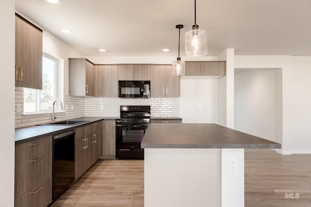 kitchen with light wood-type flooring, sink, black appliances, a kitchen island, and hanging light fixtures