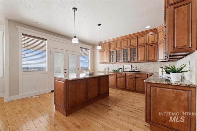 25374 W Deep Canyon Dr, Star, ID 83644 - kitchen with brown cabinetry, a center island, tasteful backsplash, light stone counters, and light wood-style floors