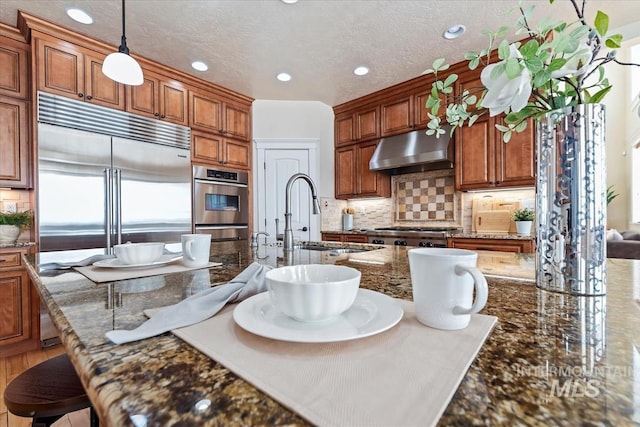 25374 W Deep Canyon Dr, Star, ID 83644 - kitchen featuring under cabinet range hood, a sink, a breakfast bar, decorative backsplash, and brown cabinetry