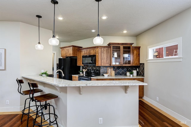 kitchen with brown cabinets, a kitchen bar, hanging light fixtures, glass insert cabinets, and black appliances