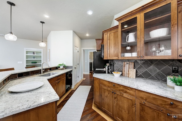 kitchen featuring glass insert cabinets, decorative light fixtures, light stone countertops, black appliances, and a sink