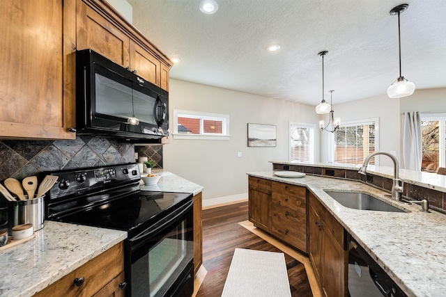 kitchen with decorative backsplash, light stone counters, decorative light fixtures, black appliances, and a sink