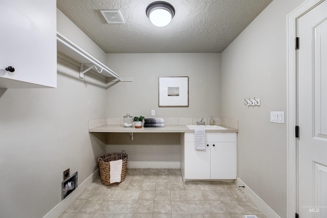 clothes washing area with cabinet space, visible vents, a sink, a textured ceiling, and baseboards