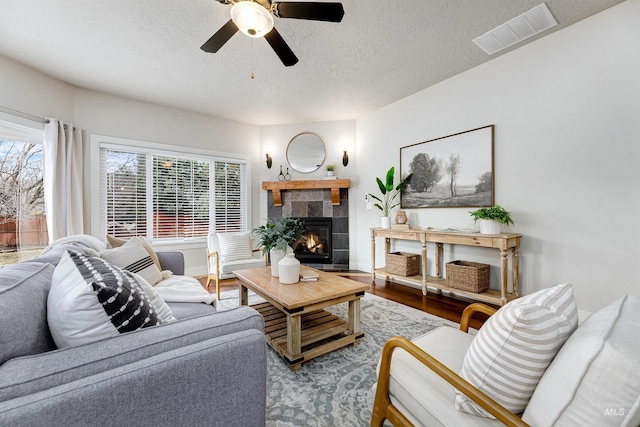 living area featuring visible vents, a fireplace, a textured ceiling, and wood finished floors