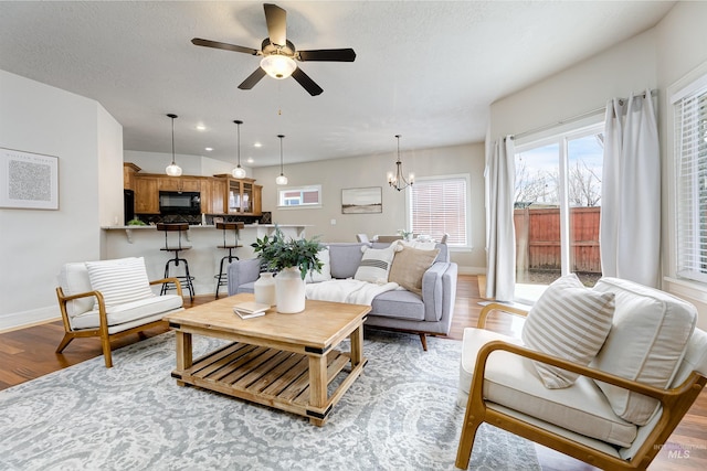 living area with recessed lighting, light wood-style floors, a textured ceiling, baseboards, and ceiling fan with notable chandelier