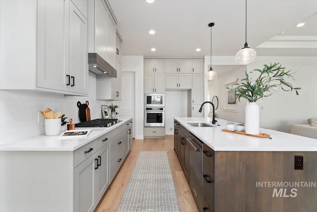 kitchen featuring a sink, light countertops, appliances with stainless steel finishes, wall chimney exhaust hood, and backsplash