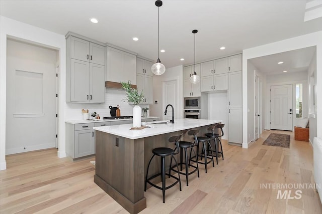 kitchen featuring a sink, light wood-style floors, backsplash, and stainless steel appliances