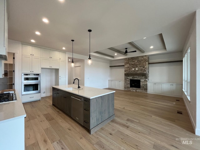 kitchen with ceiling fan, a tray ceiling, appliances with stainless steel finishes, and light wood-style flooring