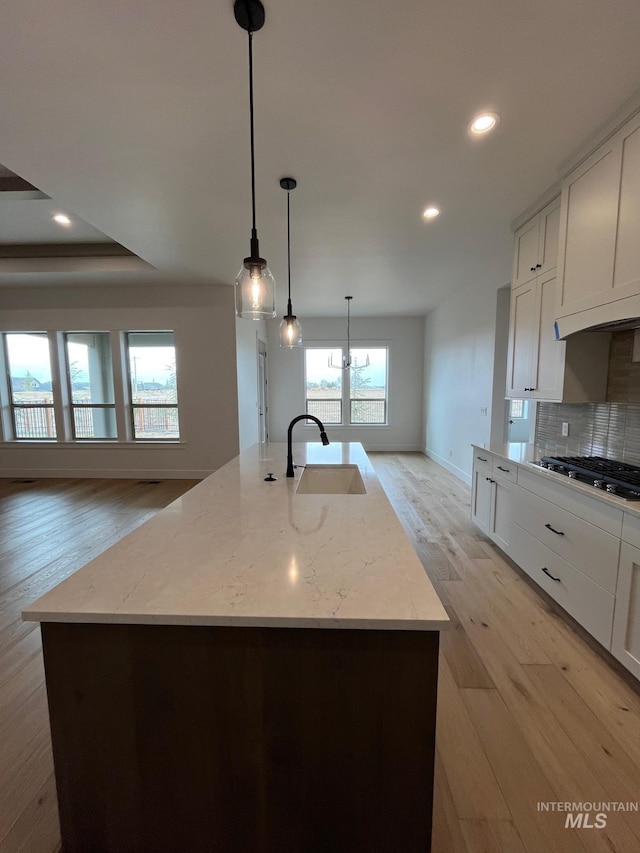 kitchen with backsplash, light stone counters, light wood-style floors, gas stovetop, and a sink