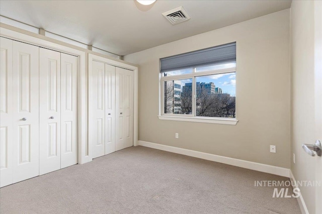 unfurnished bedroom with light carpet and two closets