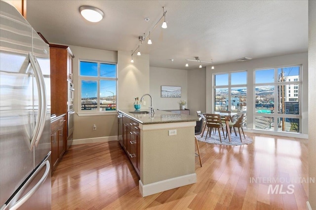 kitchen with light stone countertops, appliances with stainless steel finishes, a kitchen bar, kitchen peninsula, and sink