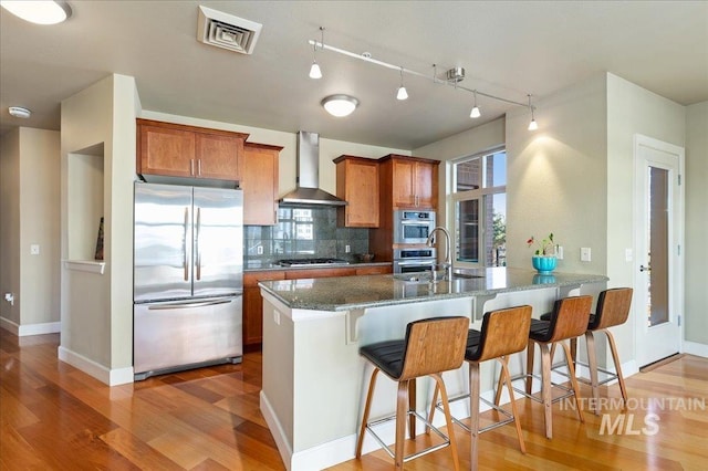 kitchen with sink, hardwood / wood-style flooring, wall chimney exhaust hood, appliances with stainless steel finishes, and tasteful backsplash