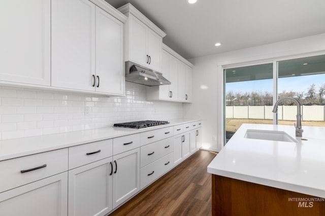 kitchen featuring light countertops, gas stovetop, under cabinet range hood, and a sink