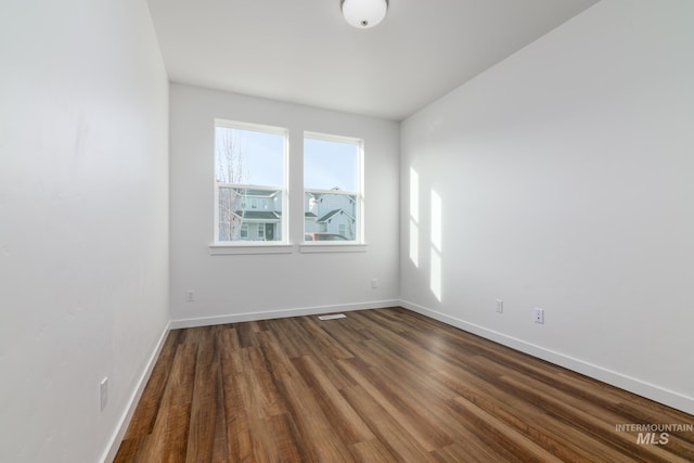 unfurnished room with visible vents, baseboards, and dark wood-style floors