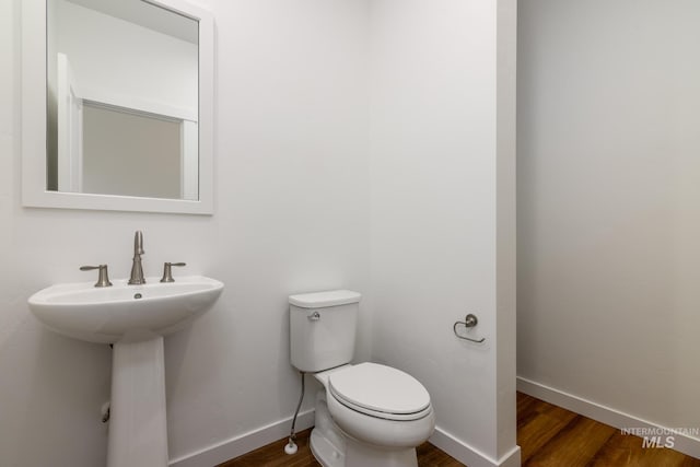 half bathroom with toilet, wood finished floors, and baseboards