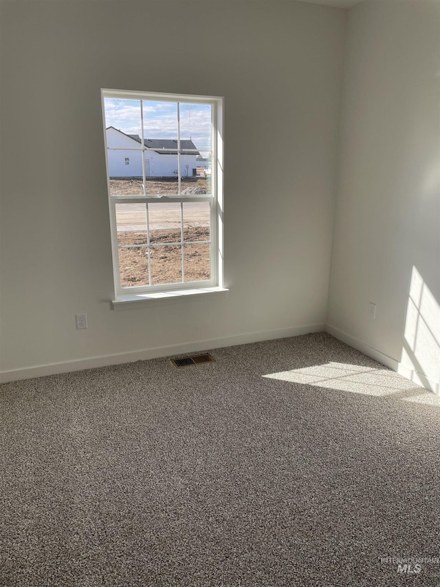 unfurnished room with carpet floors, visible vents, and baseboards