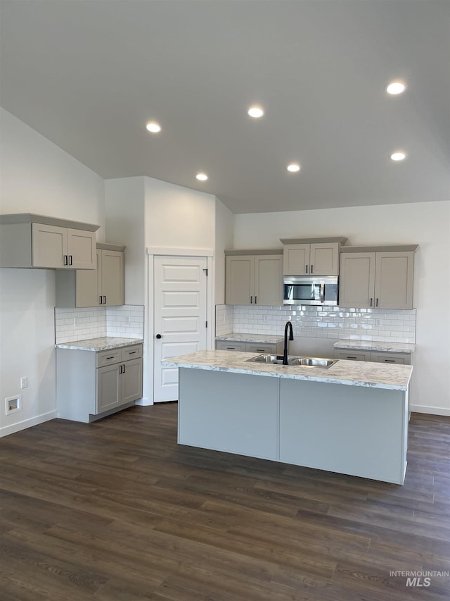 kitchen featuring a kitchen island with sink, a sink, gray cabinets, stainless steel microwave, and dark wood finished floors