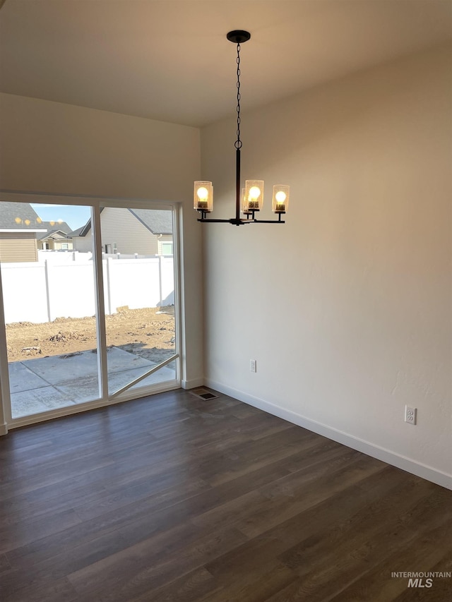 unfurnished dining area featuring dark wood-style flooring, an inviting chandelier, and baseboards