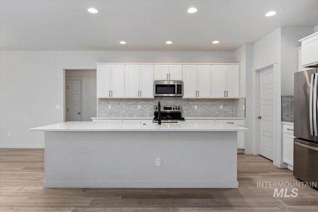kitchen featuring stainless steel appliances, decorative backsplash, light wood-style floors, white cabinets, and a kitchen island with sink