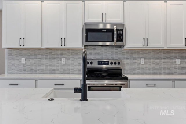 kitchen featuring white cabinetry, light stone countertops, appliances with stainless steel finishes, and decorative backsplash