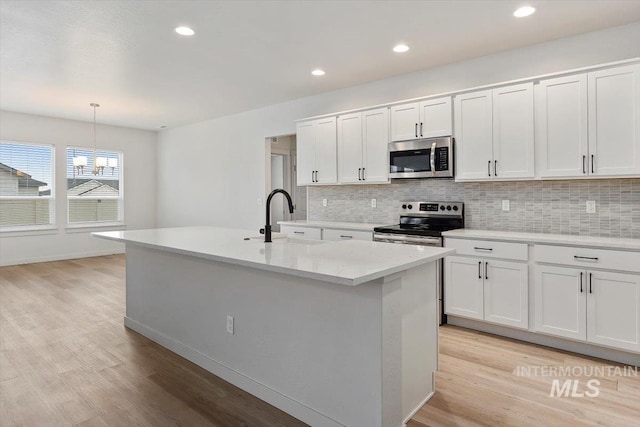 kitchen with backsplash, a sink, light wood-style floors, white cabinets, and appliances with stainless steel finishes