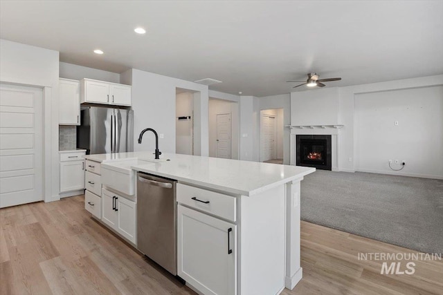 kitchen with an island with sink, a sink, a ceiling fan, white cabinetry, and appliances with stainless steel finishes