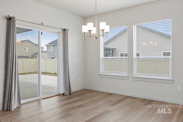 unfurnished dining area featuring baseboards, light wood-style flooring, and a notable chandelier