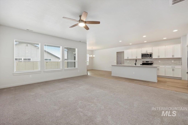 unfurnished living room with visible vents, ceiling fan, recessed lighting, a sink, and light colored carpet