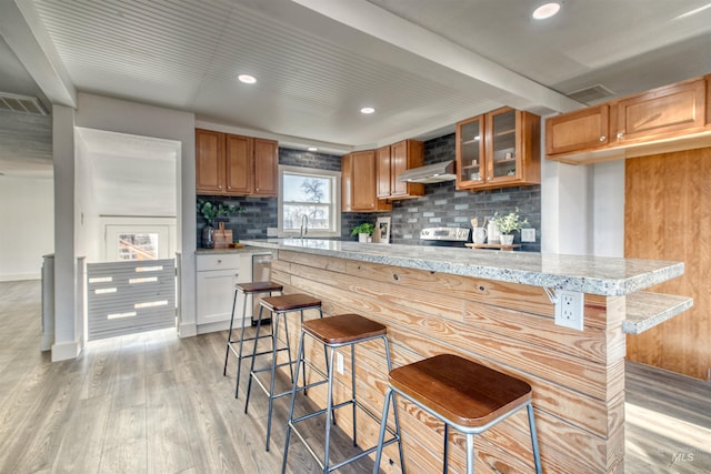 kitchen with exhaust hood, a kitchen breakfast bar, light wood-type flooring, tasteful backsplash, and light stone counters