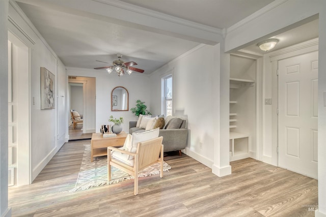 living room with built in shelves, crown molding, ceiling fan, and light wood-type flooring