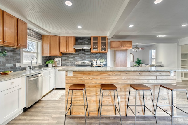 kitchen with white cabinets, stainless steel dishwasher, light stone countertops, and a breakfast bar area