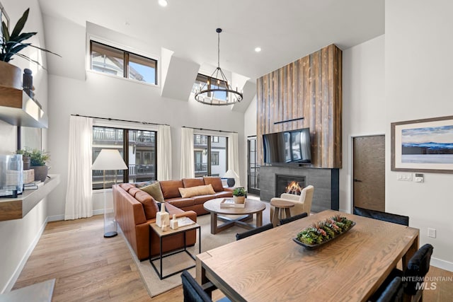 dining space featuring a towering ceiling, a fireplace, an inviting chandelier, and light hardwood / wood-style flooring