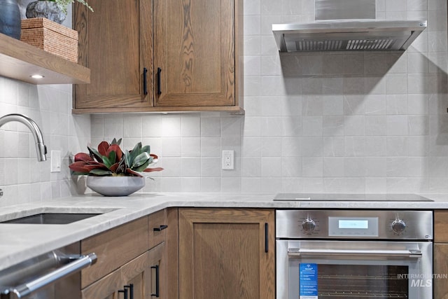 kitchen featuring stainless steel appliances, sink, light stone counters, wall chimney exhaust hood, and backsplash