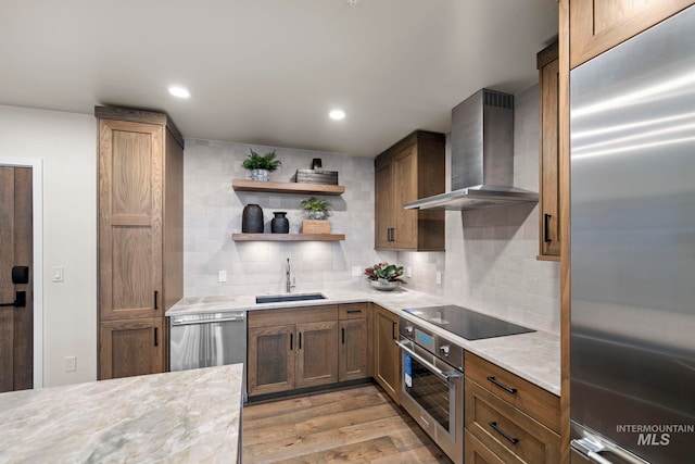 kitchen with stainless steel appliances, wall chimney range hood, light wood-type flooring, backsplash, and sink