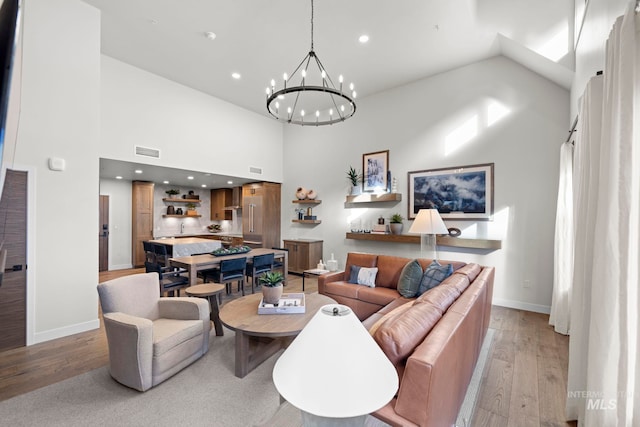 living room with a high ceiling, a chandelier, and light hardwood / wood-style flooring