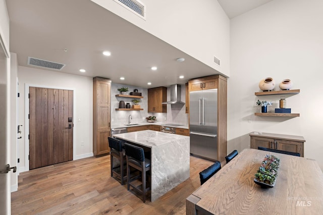 kitchen featuring wall chimney exhaust hood, light hardwood / wood-style floors, a kitchen bar, appliances with stainless steel finishes, and sink